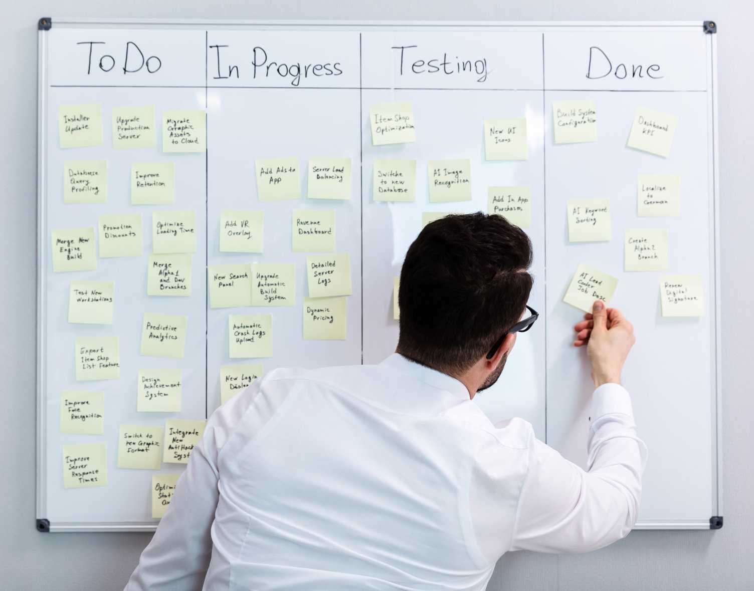Ein Mann entfernt ein Merkzettel aus der Done-Spalte des Kanban Boards